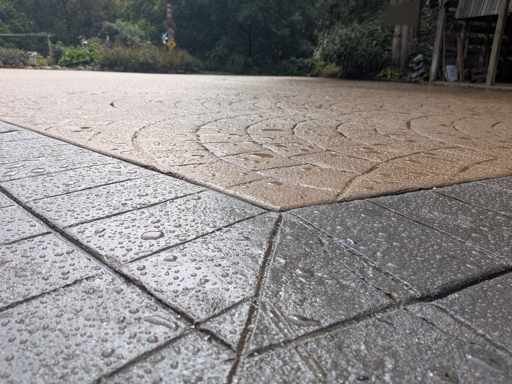 Resealed border detail: water droplets on the charcoal square-pattern border where it meets the tan fan-pattern field