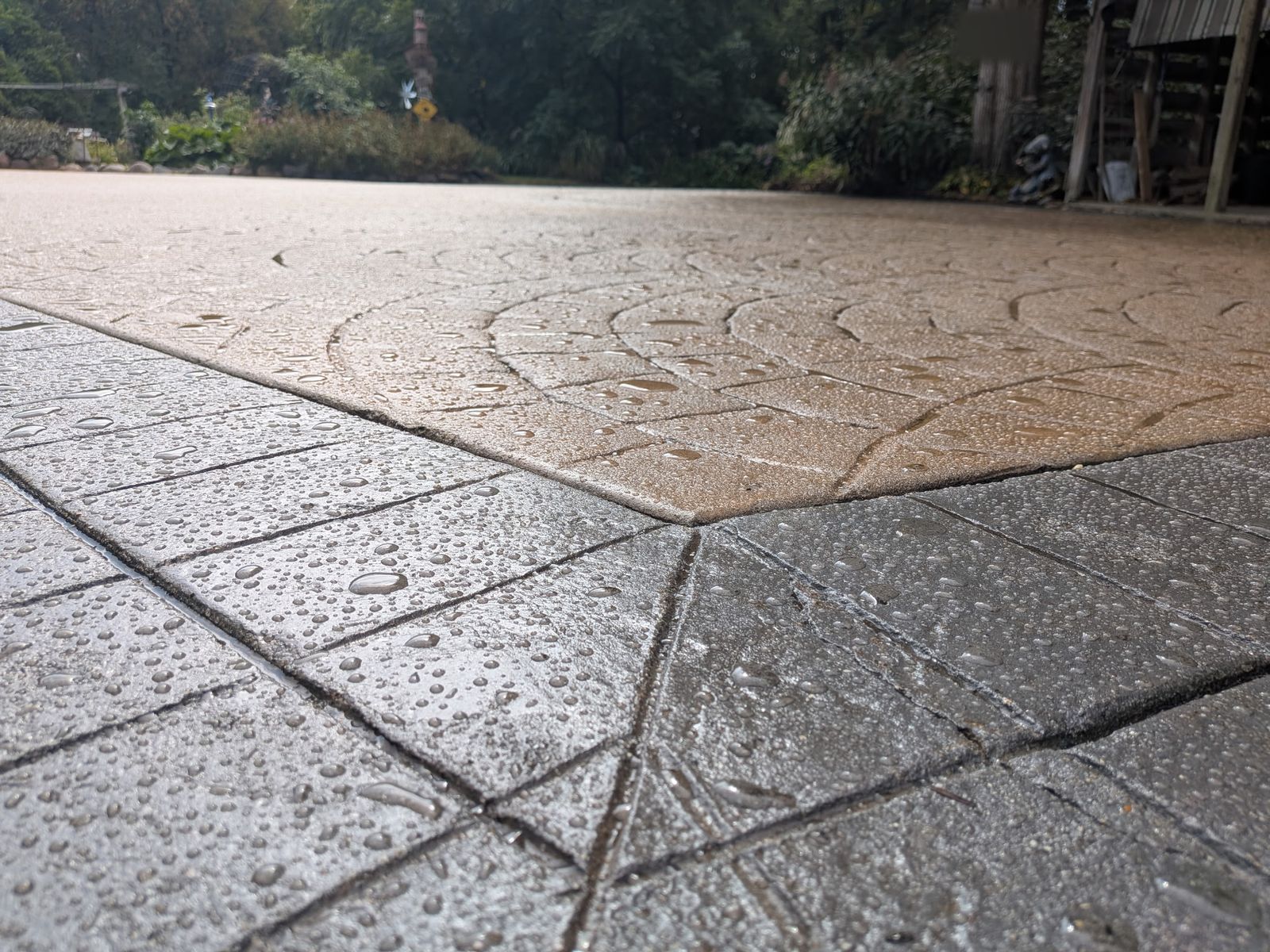 Water droplets on an existing stamped-concrete driveway after cleaning and resealing by Ironcrest Outdoor.