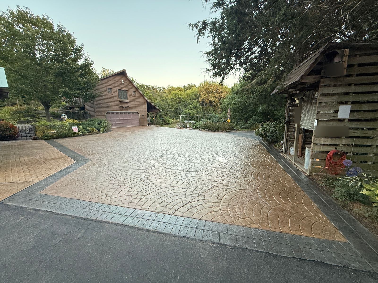 Existing stamped-concrete driveway after cleaning and resealing by Ironcrest Outdoor — a tan fan-pattern field framed by a charcoal square-pattern border